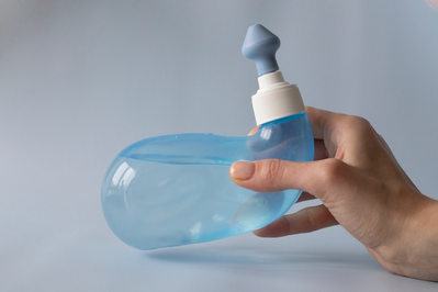 hand holding blue transparent neti pot filled with saline solution