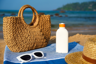 sunscreen bottle and sunglasses sitting on towel at the beach next to a basket and hat