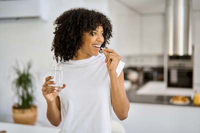 smiling, healthy woman taking a multivitamin with a glass of water