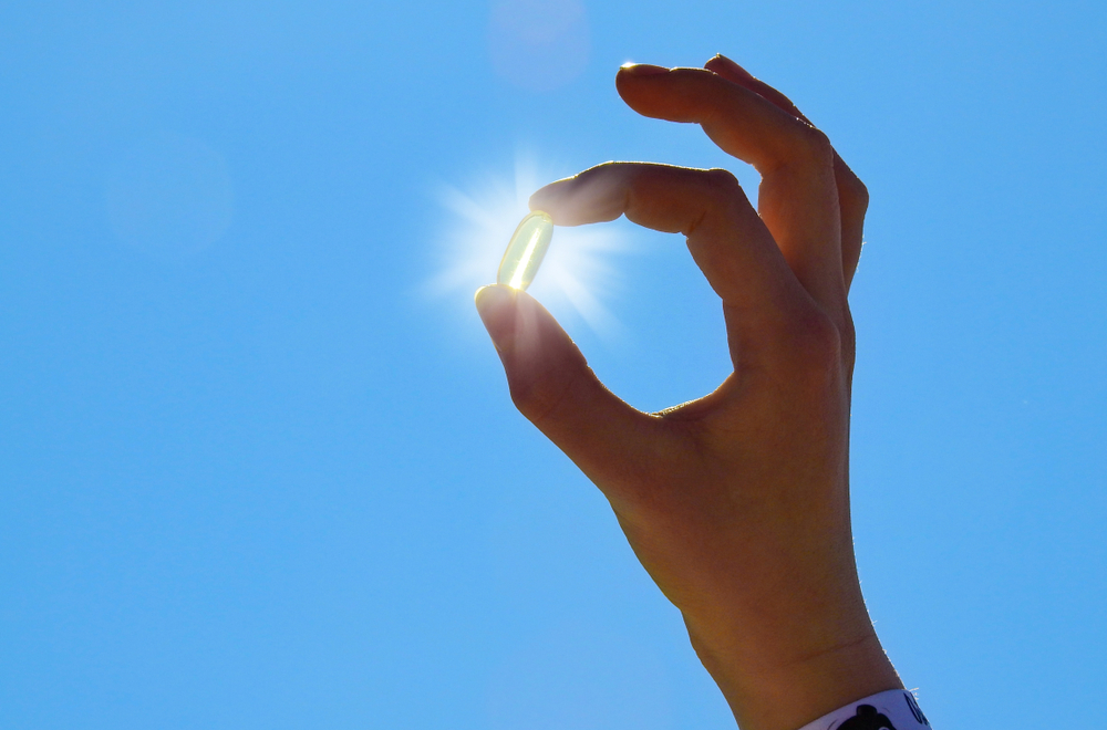 hand holding vitamin D pill up to the sun in cloudless blue sky