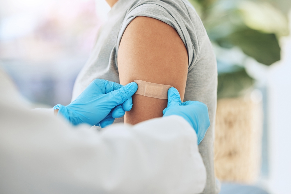 gloved hands putting bandage on arm after giving vaccine