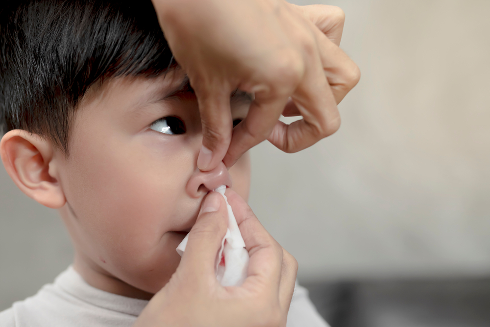 parent pinching nose and holding tissue to help little boy with nosebleed