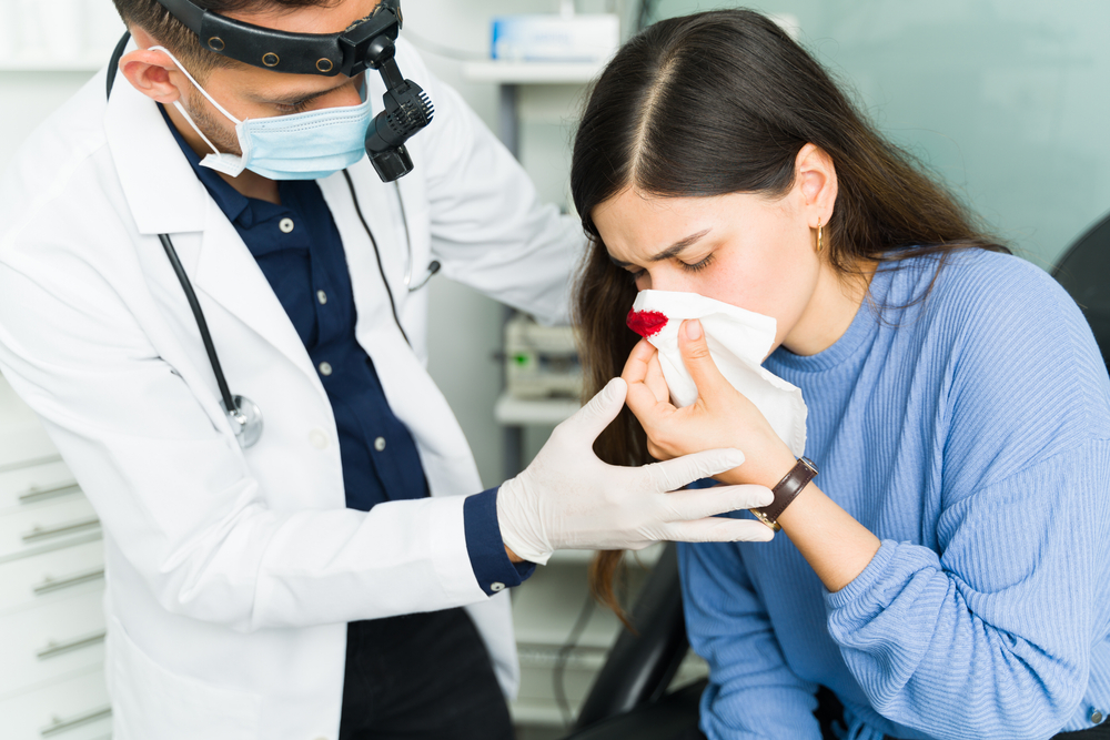 doctor helping woman stop nosbleed by leaning forward and holding tissue over nose