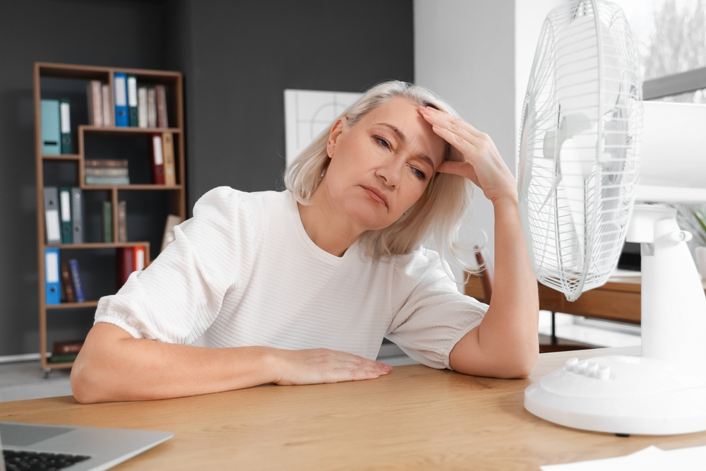 senior woman sitting in front of electric fan during hot flash