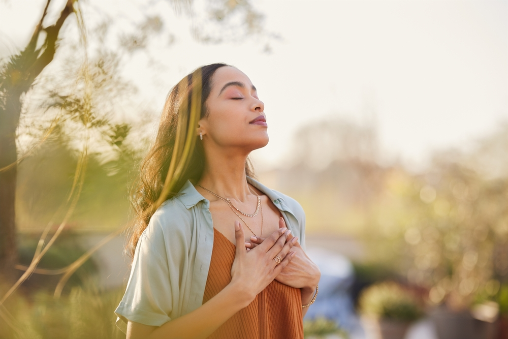 woman practicing mindfulness with eyes closed and hands on chest while standing outside